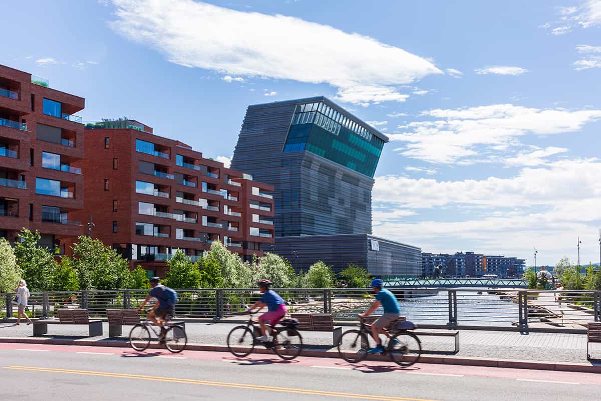 Cyclists riding along a dedicated bike path in central Oslo, with modern buildings and greenery in the background