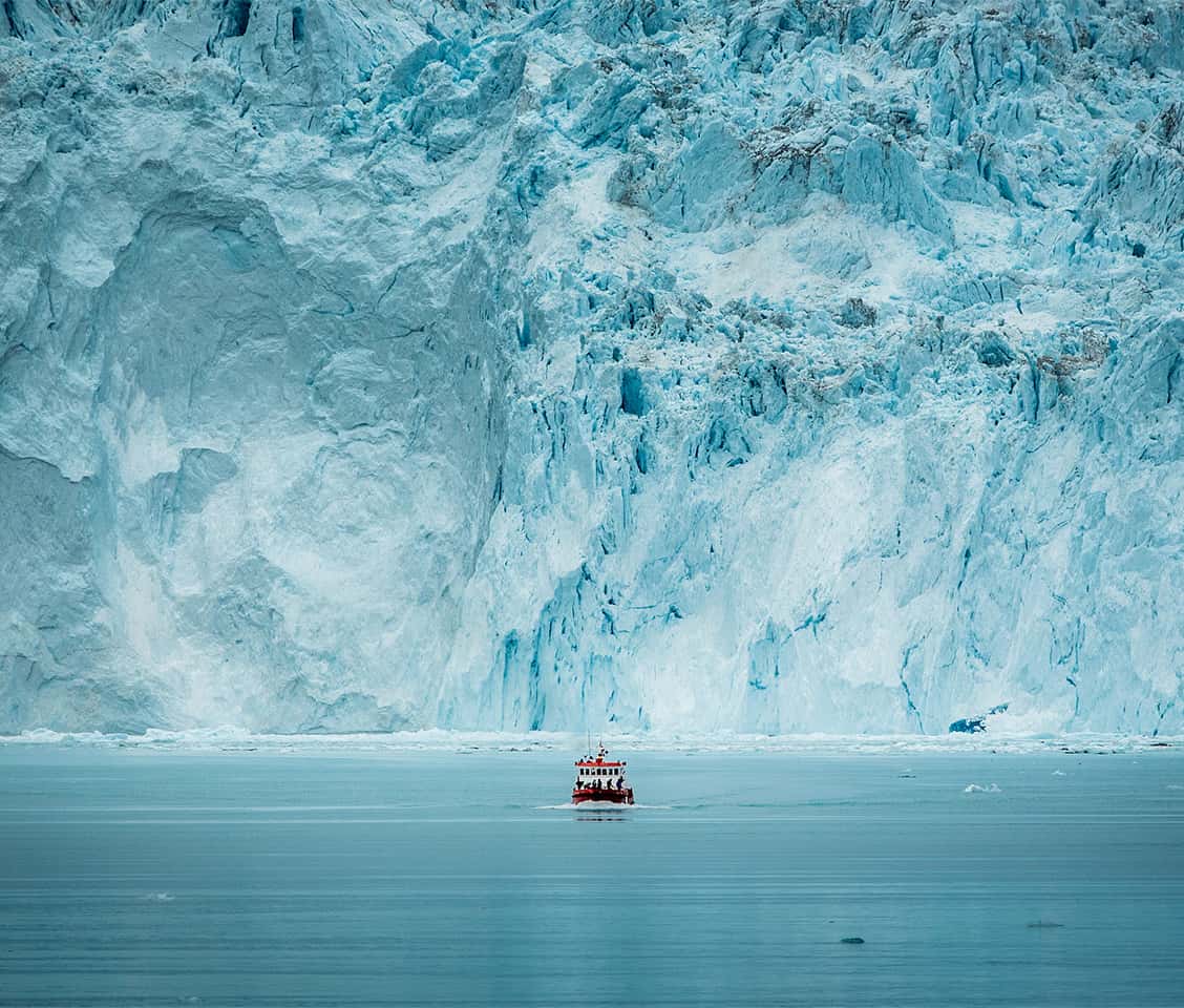 Boat in front of the huge glacier wall at the Eqi glacier in Greenland