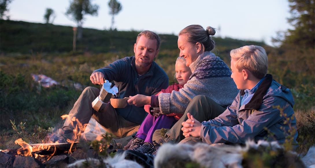 Family gathered around a bonfire in Norway, surrounded by nature and warm evening light, enjoying togetherness in a peaceful setting