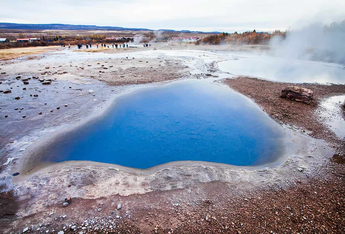 The Geysir Geothermal Area in Iceland with steaming hot springs, bubbling mud pots, and the Strokkur geyser erupting into the air