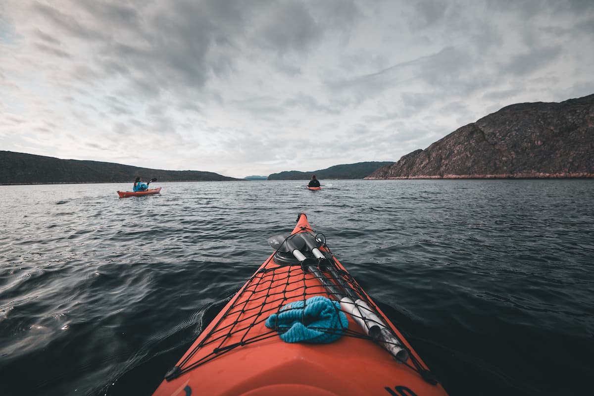 Kayakers paddling through calm Arctic waters near Aasiaat Greenland surrounded by icebergs and coastal landscapes under a clear sky