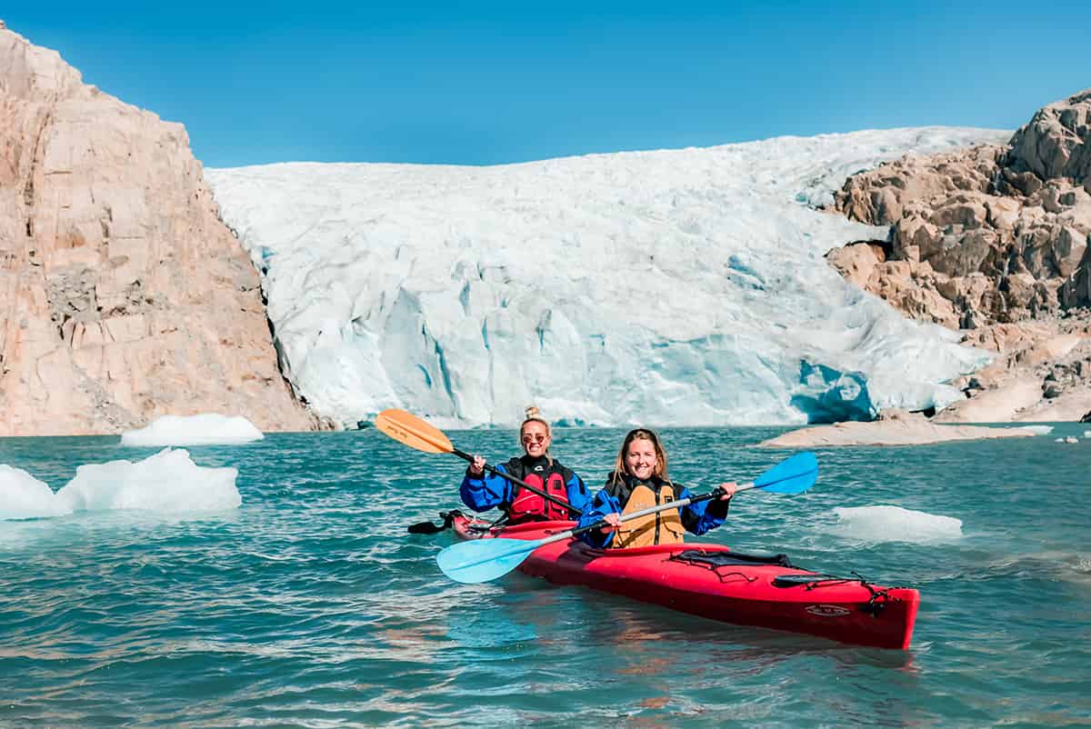 Kayak gliding across calm waters near the edge of Folgefonna glacier in Norway, with icy terrain and distant mountains under a bright sky