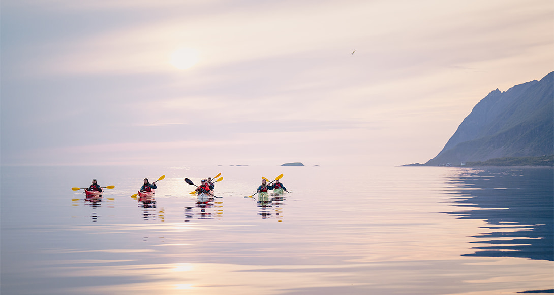Person kayaking under the midnight sun at Senja in Northern Norway, with golden light reflecting on calm waters and dramatic coastal peaks