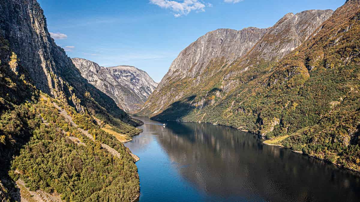 Narrow fjord flanked by steep, green mountains with calm water reflecting the sky in Nærøyfjord, Norway