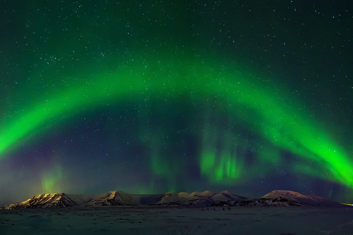 The Northern Lights glowing in green and purple hues across the night sky in Iceland above a dark, open landscape