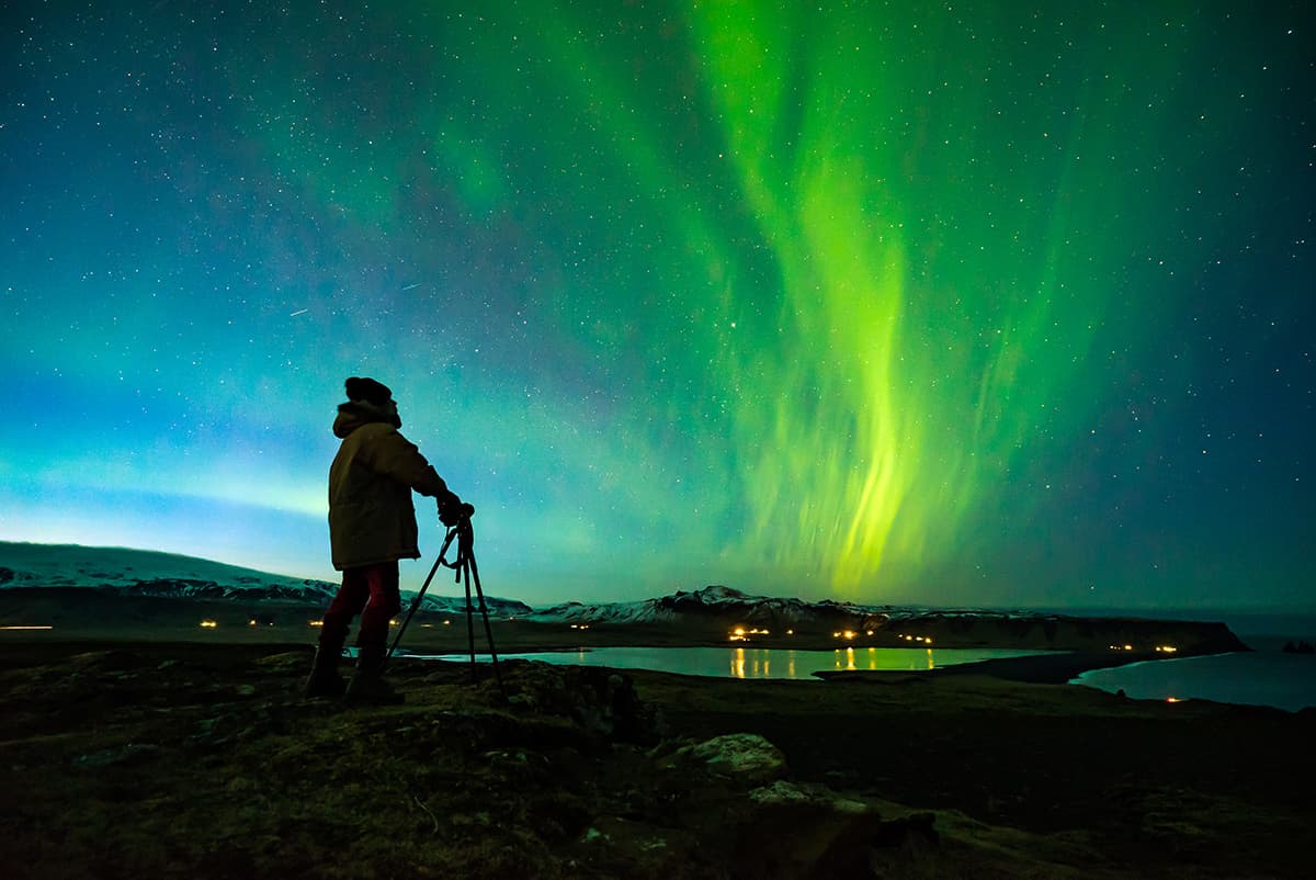 The Northern Lights illuminating the night sky in Iceland with vibrant green and purple waves above a dark, rugged landscape
