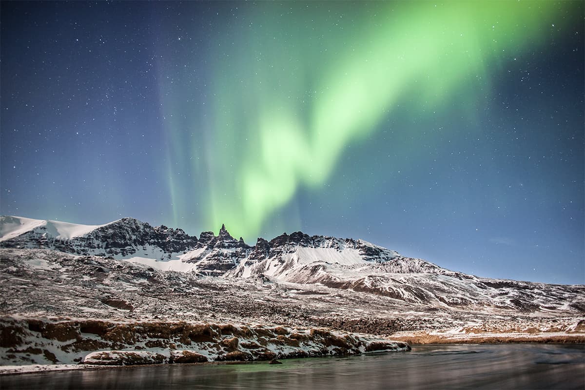Northern lights glowing in the night sky over North Iceland, with vibrant green and purple auroras above a snowy landscape
