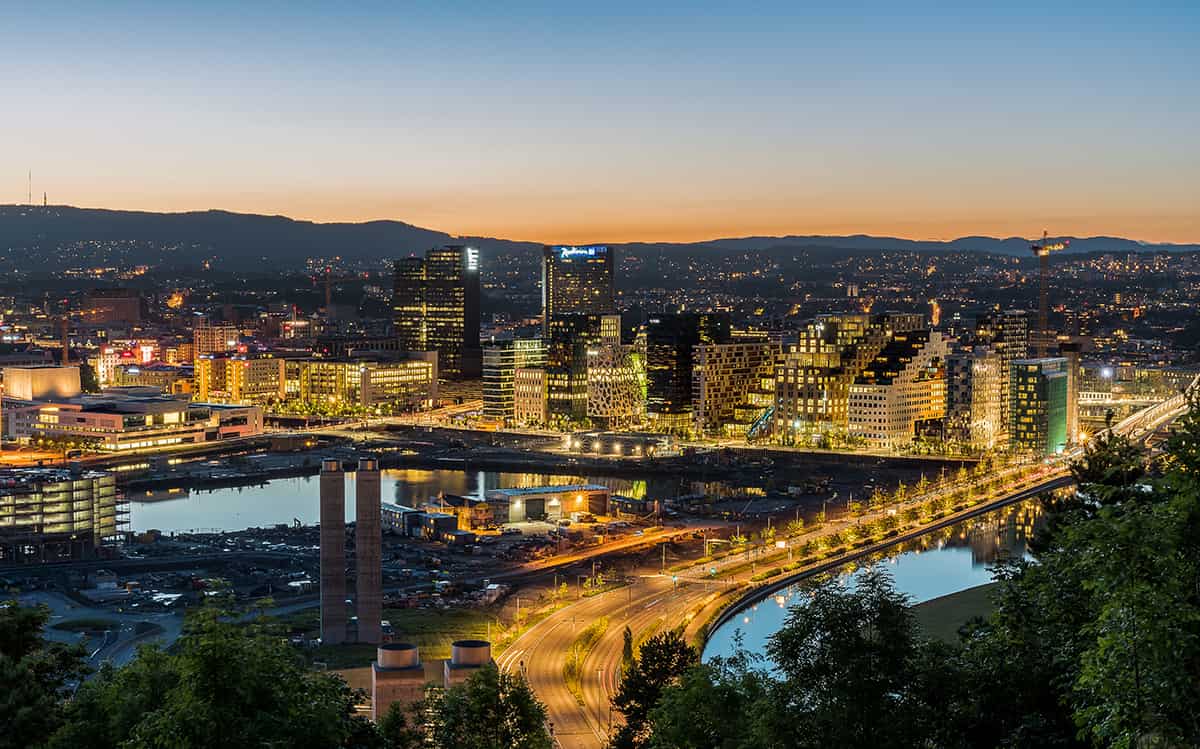 A scenic view of Oslo city center with modern architecture, historic buildings, and waterfront surroundings under a clear sky