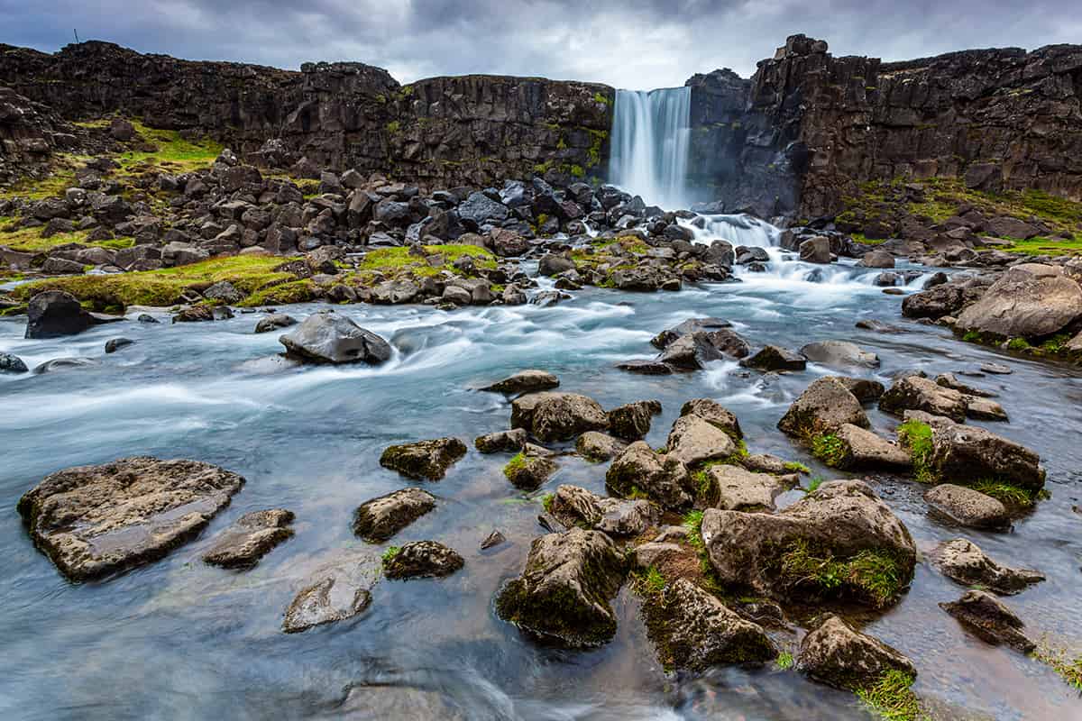 Öxarárfoss waterfall cascading over volcanic rocks in Almannagjá Gorge within Þingvellir National Park, surrounded by rugged cliffs and mossy terrain