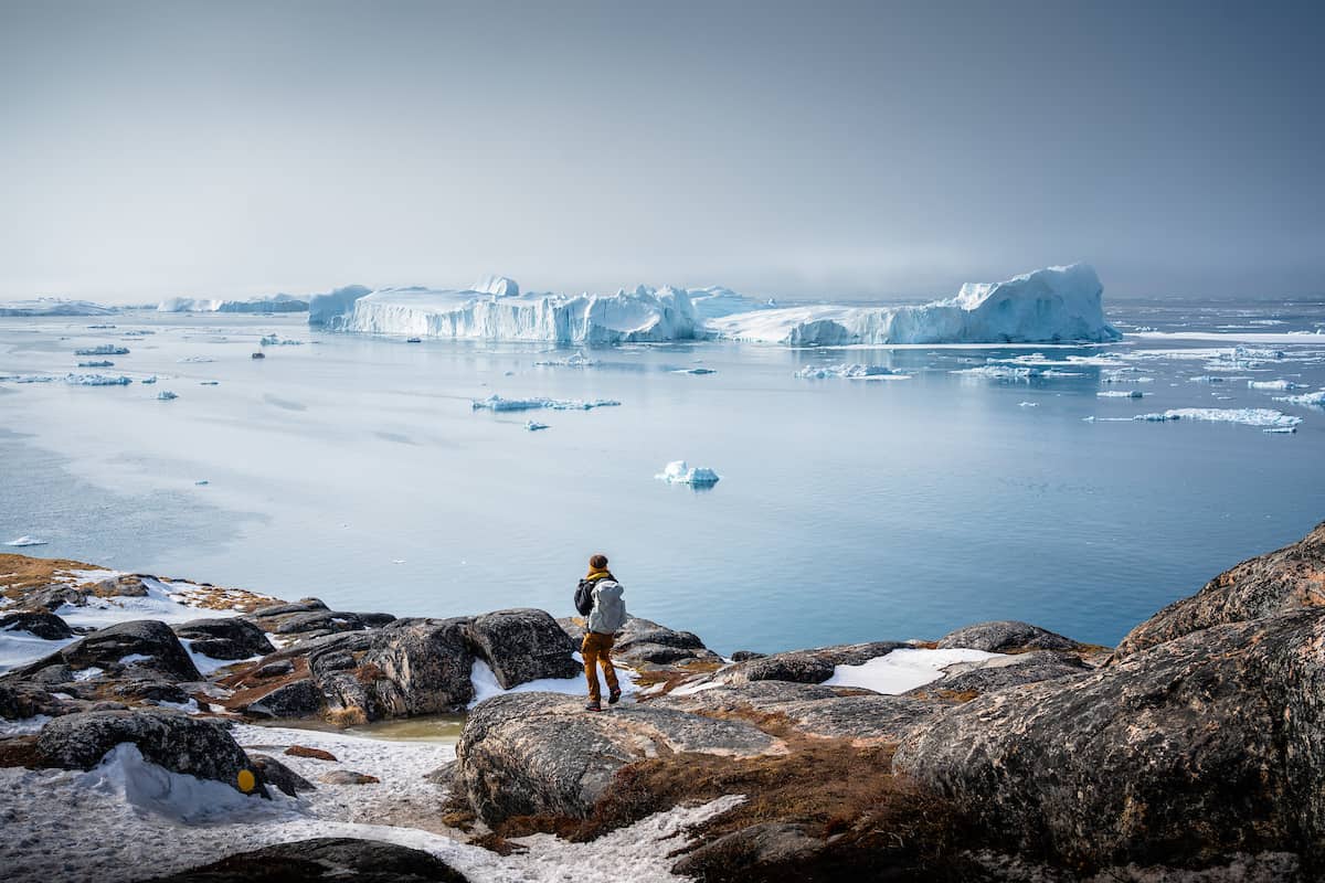 Person standing and looking out over the icefjord in Ilulissat with towering icebergs and Arctic light