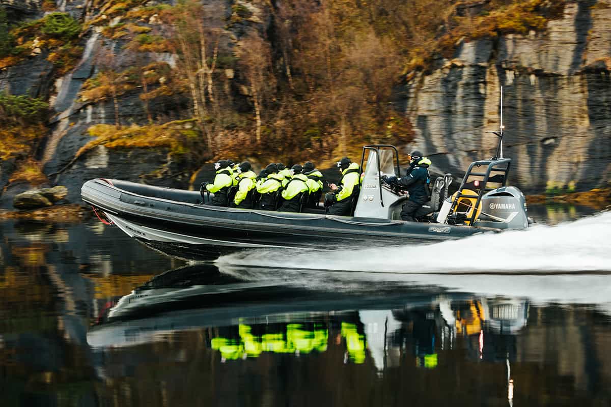 RIB boat speeding through narrow fjords in Norway surrounded by towering cliffs and deep blue water