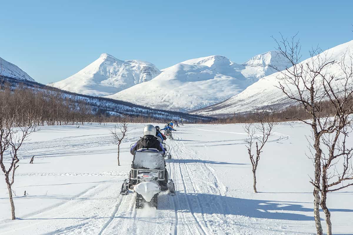 Snowmobile parked on a snowy plateau with mountains in the background and tracks in the fresh snow