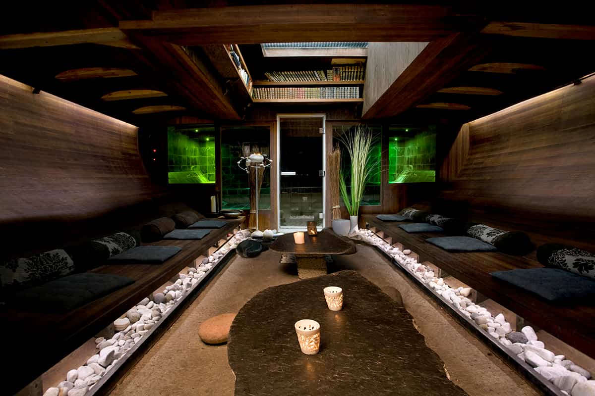 Floating spa boat with a wooden deck and hot tubs, anchored in calm Nordic waters with scenic surroundings
