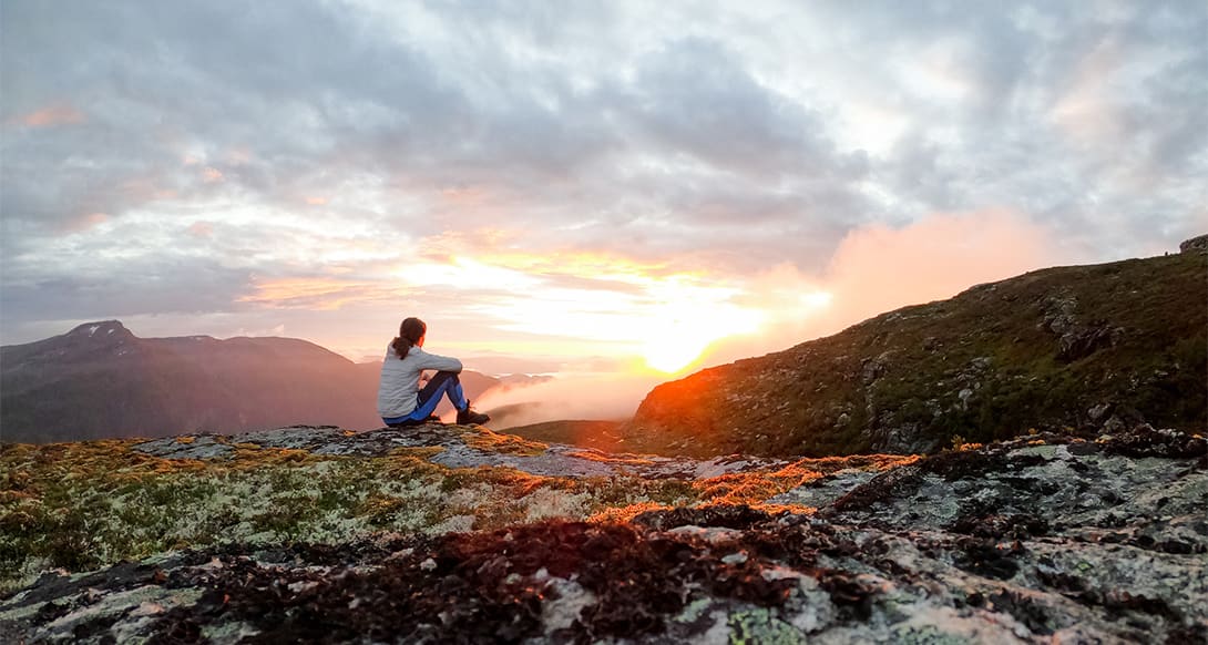 Sunset over Trollheimen Mountain in Norway, casting golden light across rugged peaks, valleys, and a peaceful alpine landscape