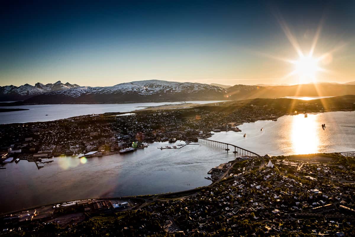 Coastal city of Tromsø with colorful buildings, surrounding hills, and calm Arctic waters under a clear sky