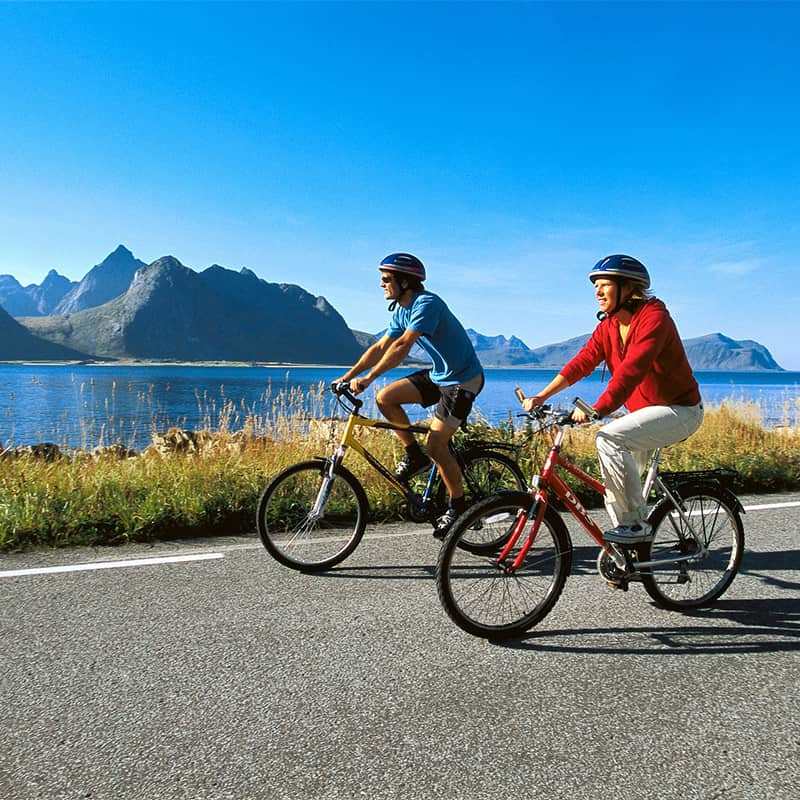 Cycling along a scenic road in Lofoten, Norway, surrounded by dramatic peaks and coastal views in a landscape of rugged Arctic beauty