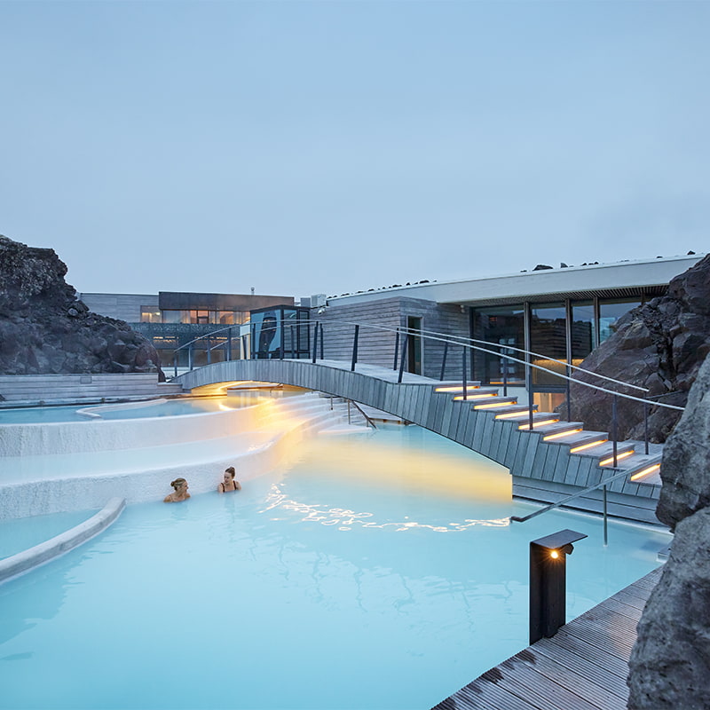 People relaxing in the warm geothermal waters of the Blue Lagoon Iceland surrounded by black lava rocks and soft steam in a peaceful setting