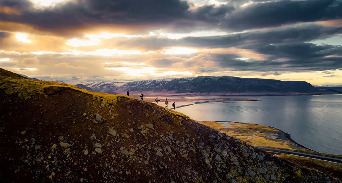 Hikers climbing a mountain with ocean and distant peaks in the background in Iceland creating a sense of remote adventure and freedom
