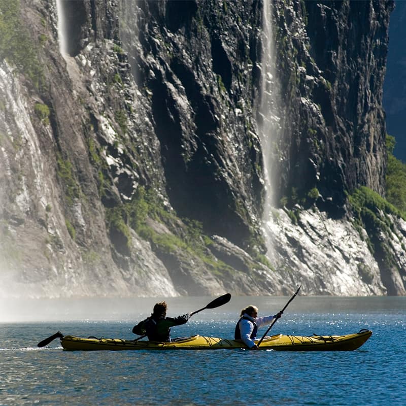 Kayaking on the calm waters of Geirangerfjord in Norway, surrounded by steep cliffs and waterfalls in a serene and scenic fjord landscape