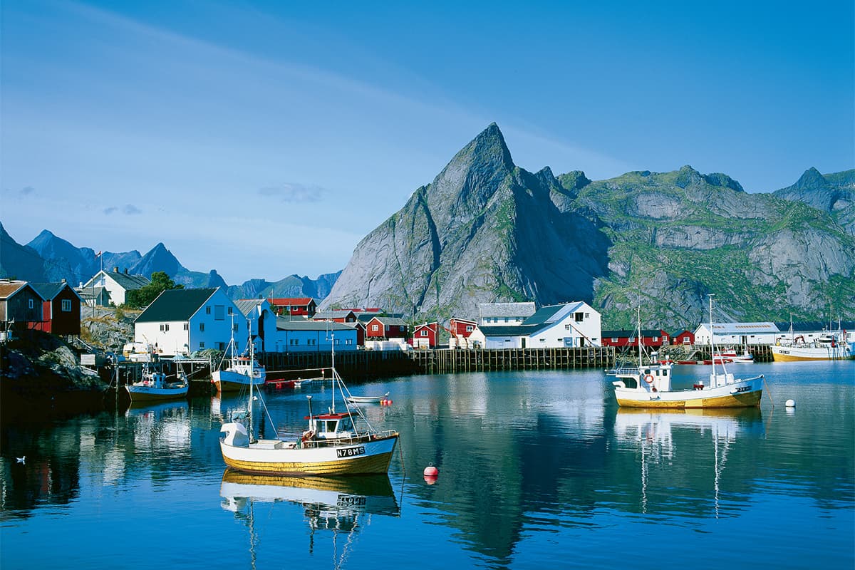 colorful houses and boats in a calm harbor with mountain backdrop in Lofoten Norway under clear blue sky