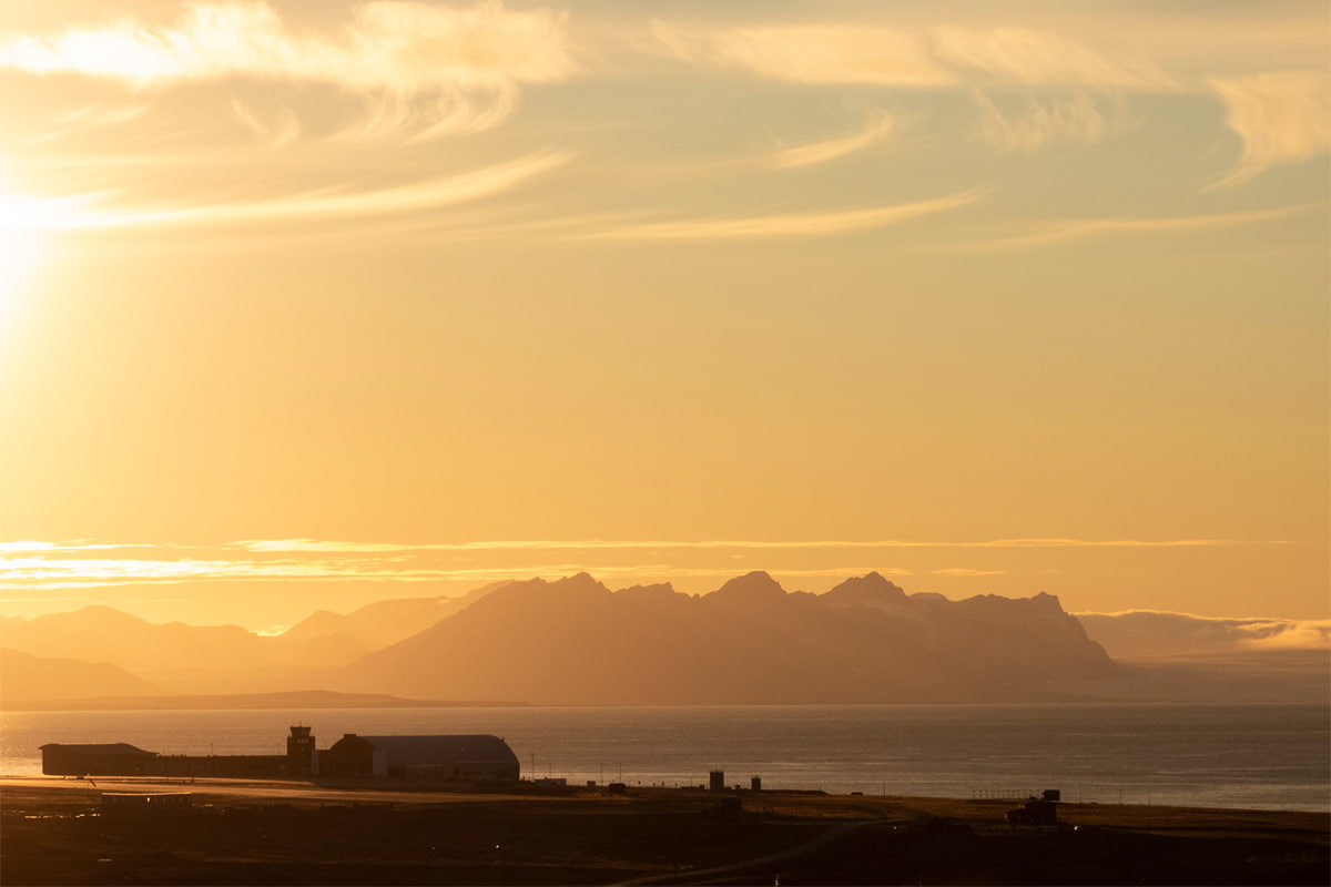 Svalbard Airport under glowing midnight sun with golden light reflecting off the tarmac and surrounding arctic landscape