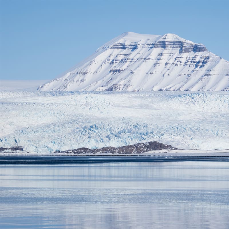 Snowcapped Terrierfjellet rising above the icy expanse of Nordenskiöldbreen in Svalbard under a soft arctic sky