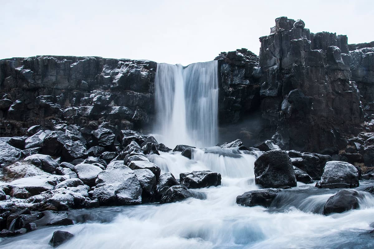 Scenic view of Thingvellir in Iceland with rocky terrain river and rift valley under clear sky and distant mountains