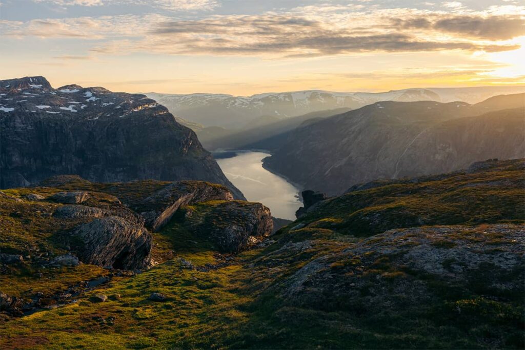 Evening view from Trolltunga in Norway with soft golden light over dramatic cliffs deep fjord and distant mountains in a tranquil atmosphere