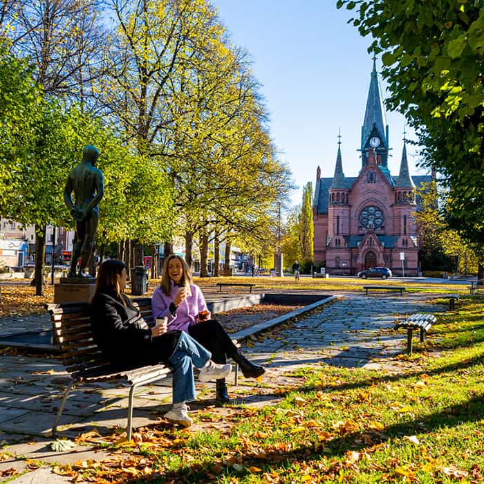Two women enjoying coffee on a bench in Sagene, Oslo, Norway on a sunny day