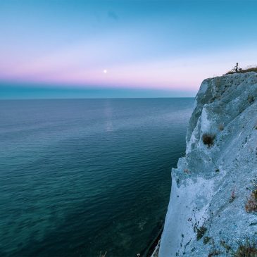 White chalk cliffs of Møns Klint on the south coast of Denmark rising above the Baltic Sea with lush green forest above and clear blue water below