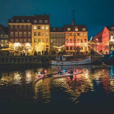 Colorful historic buildings and moored boats along the Nyhavn canal in Copenhagen Denmark with reflections on the water and a lively harbor atmosphere